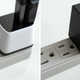 The Human Things Genki Covert Dock Mini shown plugged into a power bar and blocking a neighboring outlet, while the Nintendo Switch OLED's power adapter does not.